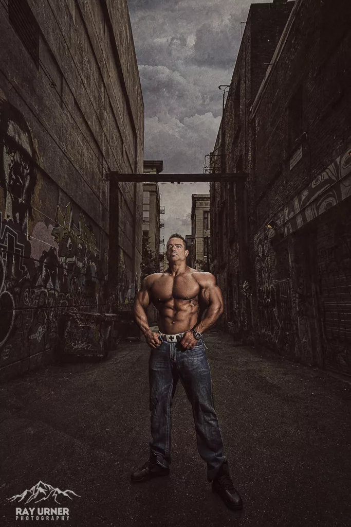 IFBB pro bodybuilder posing shirtless in a Vancouver back alley