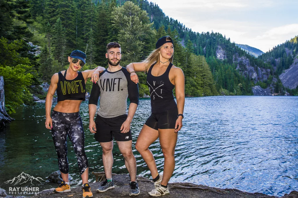 Three athletes posing at a lake